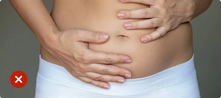 Person holding their stomach with a red cross mark, indicating discomfort or illness.