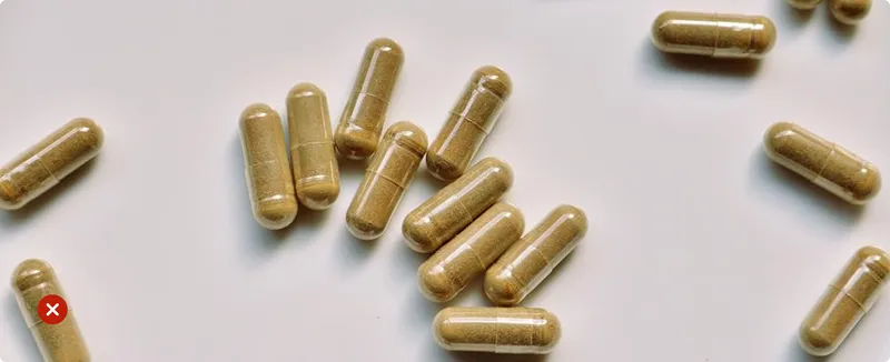 Brown capsules on a white background with one capsule marked by a red 'X'.