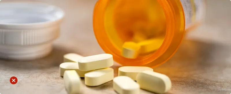 Yellow pills spilling out of an orange prescription bottle on a wooden surface.
