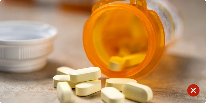 Open prescription bottle with yellow pills on a wooden surface