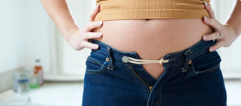 Person wearing a yellow top and blue jeans with a visible baby bump, indicating pregnancy.