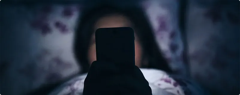 Person holding a smartphone in a dimly lit room with floral curtains.