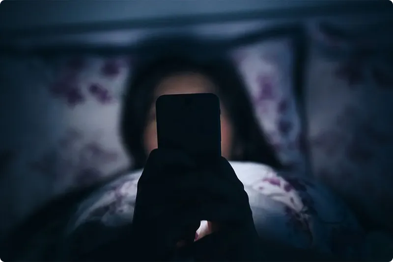 Person using a smartphone in bed under a blanket