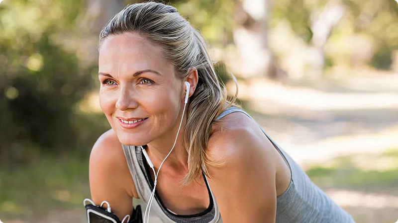 Woman exercising outdoors with earphones, smiling.